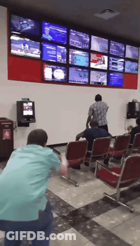 A Man In A Blue Shirt Stands In Front Of A Wall With Lots Of Tv Screens GIF