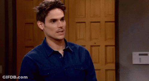 A Man In A Blue Shirt Stands In Front Of A Wooden Door GIF