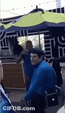 A Man In A Blue Shirt Stands Under An Umbrella GIF