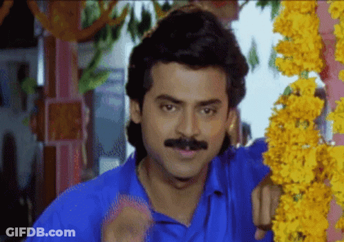 A Man In A Blue Shirt With A Mustache Is Standing In Front Of Flowers GIF