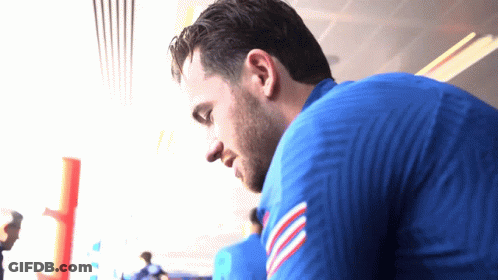 A Man In A Blue Shirt With A Red White And Blue Stripe On The Sleeve Looks Down GIF