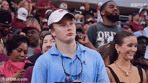 A Man In A Blue Shirt With The Letter A On It Sits In A Crowd GIF