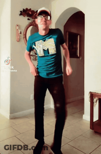 A Man In A Blue Shirt With The Letter M On It Is Dancing In A Hallway GIF