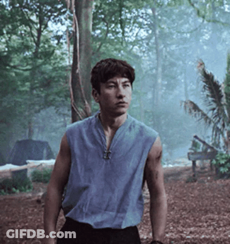A Man In A Blue Sleeveless Shirt Is Standing In The Woods GIF
