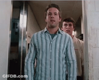 A Man In A Blue Striped Shirt Stands In A Hallway GIF