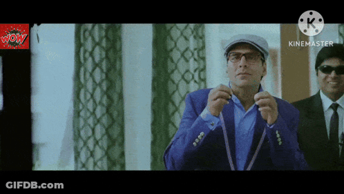 A Man In A Blue Suit Adjusts His Tie In Front Of A Screen That Says Kinemaster GIF