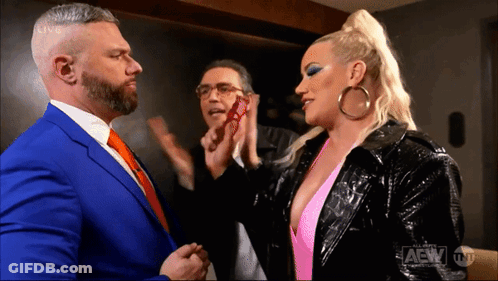 A Man In A Blue Suit And A Woman In A Pink Top Are Standing Next To Each Other In A Room . GIF