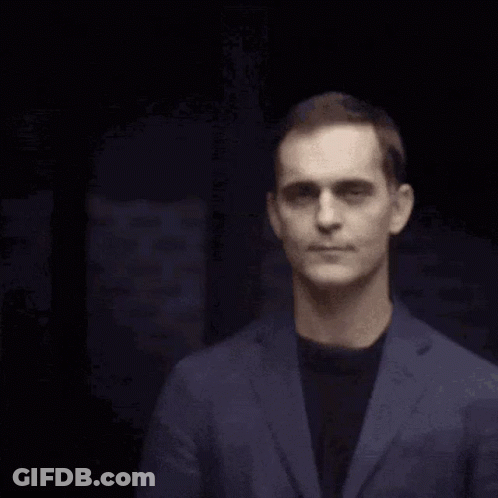 A Man In A Blue Suit And Black Shirt Is Smiling GIF