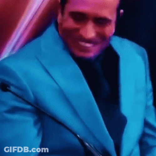 A Man In A Blue Suit And Black Tie Is Smiling While Holding A Microphone . GIF