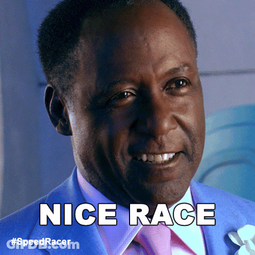 A Man In A Blue Suit And Pink Tie Is Smiling And Says Nice Race GIF