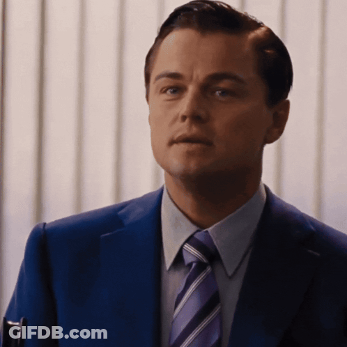 A Man In A Blue Suit And Purple Tie Looks At The Camera GIF