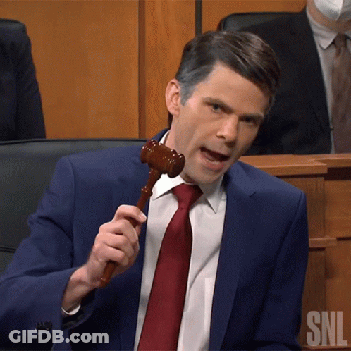 A Man In A Blue Suit And Red Tie Is Holding A Wooden Gavel With Snl Written On It GIF