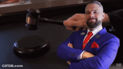 A Man In A Blue Suit And Red Tie Stands In Front Of A Judge 'S Gavel With The Number 113 On It GIF
