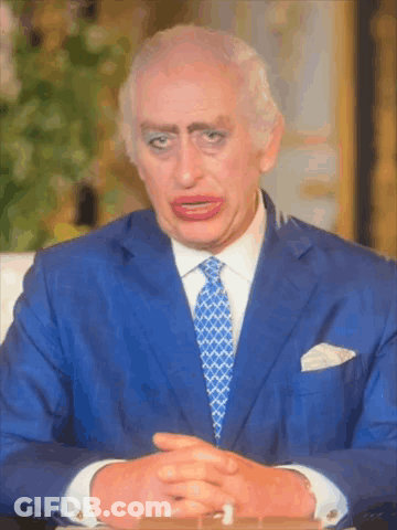 A Man In A Blue Suit And Tie Is Sitting At A Table GIF