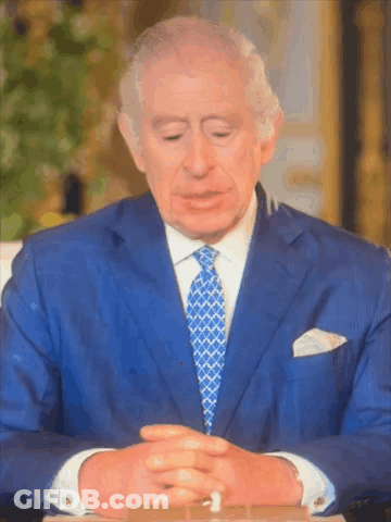 A Man In A Blue Suit And Tie Is Sitting At A Table With His Eyes Closed GIF
