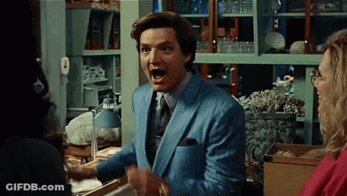 A Man In A Blue Suit And Tie Is Standing In Front Of A Woman In A Room . GIF