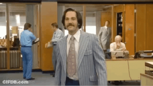 A Man In A Blue Suit And Tie Is Walking Through An Office . GIF