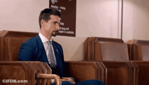 A Man In A Blue Suit And Tie Sits In Front Of A Sign That Says Monday - Friday GIF