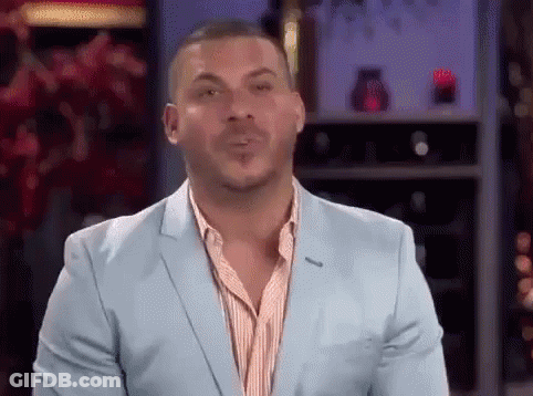 A Man In A Blue Suit Is Blowing A Kiss While Standing In Front Of A Wine Rack . GIF