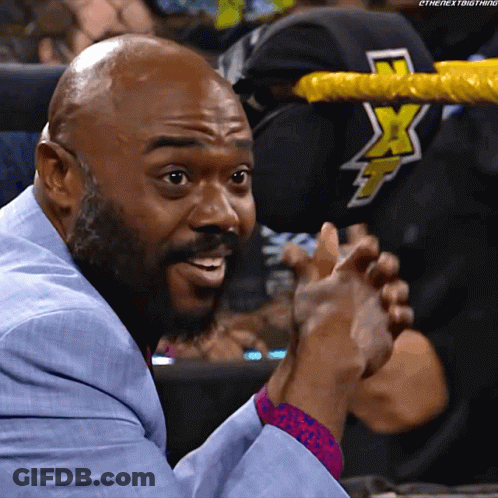 A Man In A Blue Suit Is Clapping In Front Of A Wrestling Ring With The Letters X On It GIF