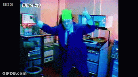 A Man In A Blue Suit Is Dancing In Front Of A Sign That Says Bbc V1 GIF