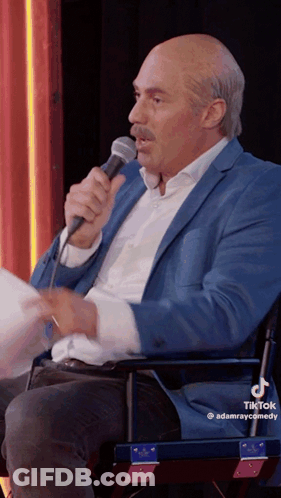 A Man In A Blue Suit Is Holding A Microphone In His Hand GIF