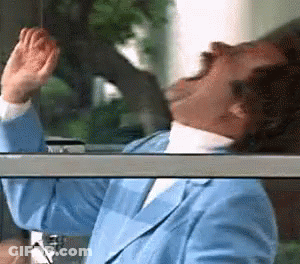 A Man In A Blue Suit Is Looking Out A Window With His Hands In The Air . GIF