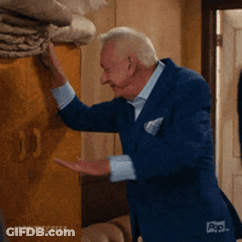 A Man In A Blue Suit Is Reaching For Something On A Wall .. GIF
