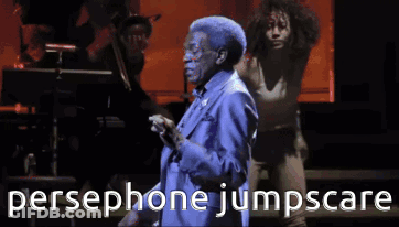 A Man In A Blue Suit Is Singing Into A Microphone With The Words Persephone Jumpscare Behind Him GIF