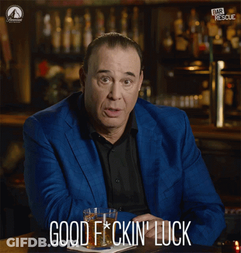 A Man In A Blue Suit Is Sitting At A Bar Holding A Glass Of Whiskey And Says Good F * Cking Luck GIF