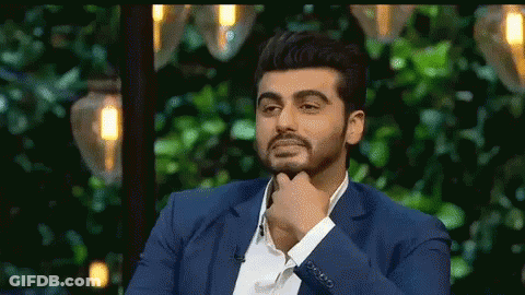 A Man In A Blue Suit Is Sitting In Front Of A Green Background With His Hand On His Chin . GIF