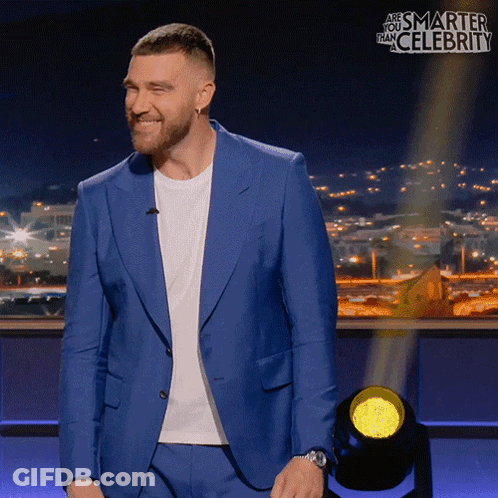 A Man In A Blue Suit Is Smiling In Front Of A Sign That Says " And Smarter Than Celebrity " GIF