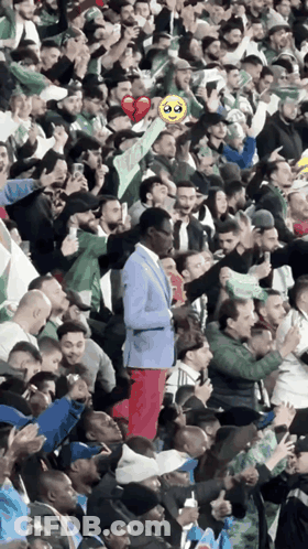 A Man In A Blue Suit Is Standing In A Crowd Of People GIF