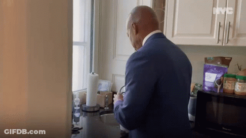 A Man In A Blue Suit Is Standing In A Kitchen With A Bag Of Purple Powder On The Counter .. GIF