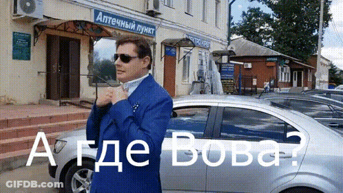 A Man In A Blue Suit Is Standing In Front Of A Building That Says " Аптечный Пункт " On It GIF