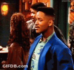 A Man In A Blue Suit Is Standing In Front Of A Woman In A Bar . GIF