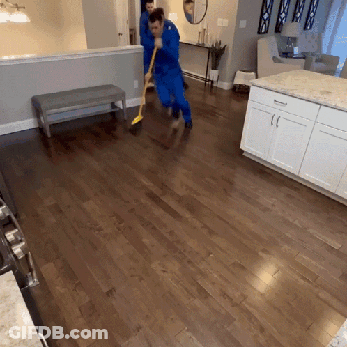 A Man In A Blue Suit Is Sweeping The Floor In A Kitchen GIF