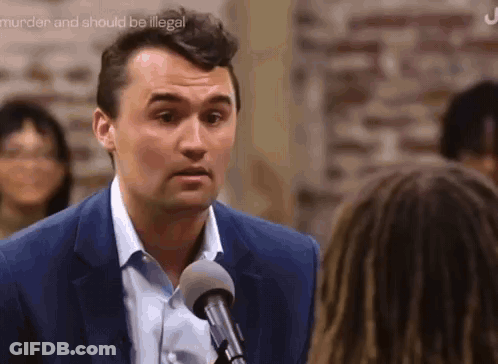 A Man In A Blue Suit Is Talking Into A Microphone While A Woman Looks On . GIF