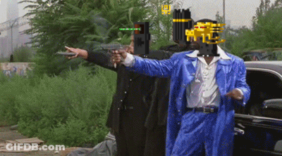 A Man In A Blue Suit Points A Gun At Another Man In A Black Suit GIF