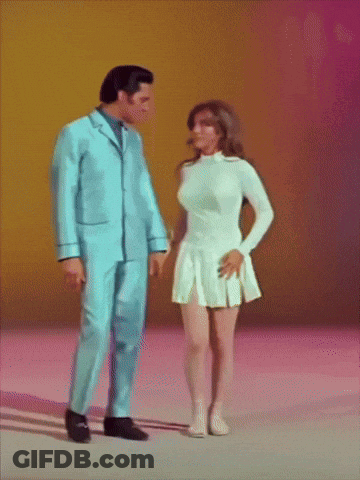 A Man In A Blue Suit Stands Next To A Woman In A White Skirt GIF