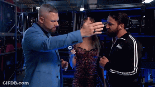 A Man In A Blue Suit Talks To A Woman And Another Man In A Black Jacket With The Word Mele On The Front GIF