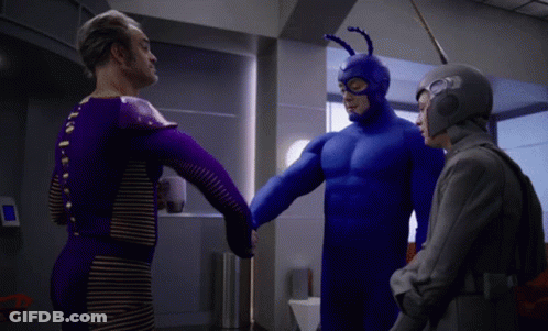 A Man In A Blue Superhero Costume Is Shaking Hands With Two Other Men GIF