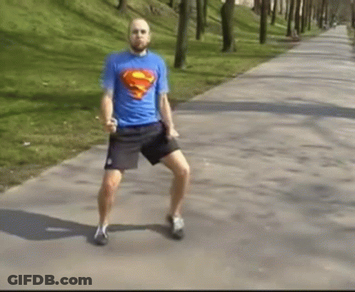 A Man In A Blue Superman Shirt Is Dancing On A Sidewalk . GIF
