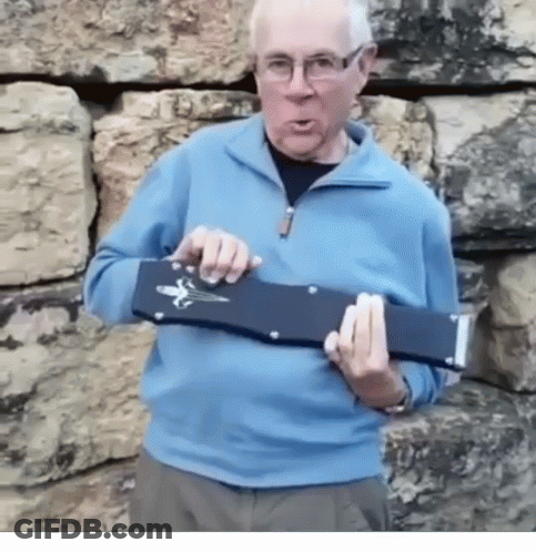 A Man In A Blue Sweater And Glasses Is Holding A Black Object In His Hands GIF