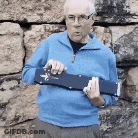 A Man In A Blue Sweater And Glasses Is Holding A Blue Object In His Hands . GIF