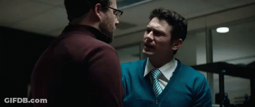 A Man In A Blue Sweater And Tie Is Talking To Another Man With The Word Haters Behind Him GIF