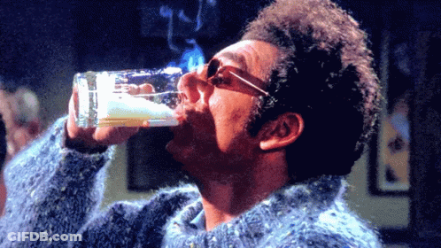 A Man In A Blue Sweater Drinks From A Glass GIF