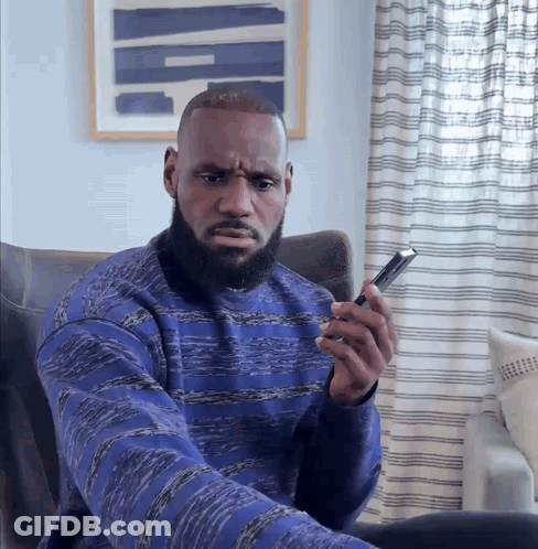 A Man In A Blue Sweater Holds A Cell Phone GIF