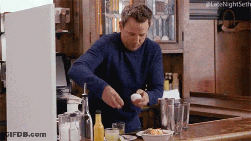 A Man In A Blue Sweater Is Cracking An Egg On A Kitchen Counter GIF