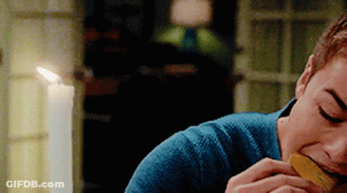 A Man In A Blue Sweater Is Eating A Piece Of Food In Front Of A Lit Candle . GIF